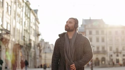 A Happy Bearded Man is Listening to Music and Walking Around the City Center