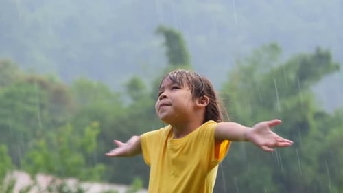 Cute little girl having fun catching rain drops. Kids play in summer rain. Child playing outdoor.
