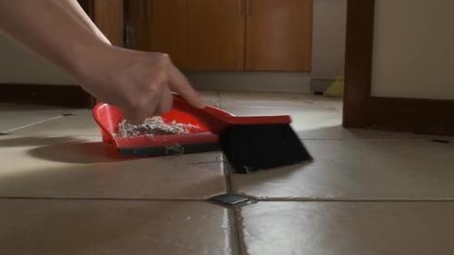 Woman Sweeping Dust into Red Dustpan on Floor