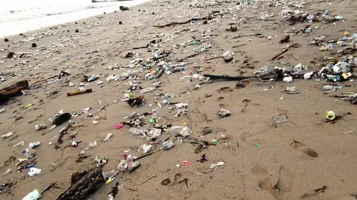 Close shot of plastic garbage on a sandy beach, polluted ocean washing out trash to the shore