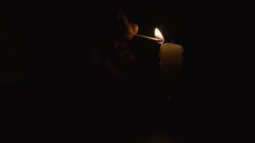 Hand Lights Candle in Dark Room with Match
