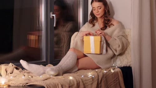 Young Woman Opens Christmas Gift on Window Seat