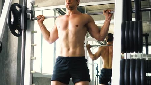 Muscular Man Doing Barbell Squat Exercise on Machine at the Gym