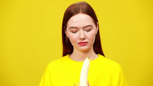 Auburn Haired Woman Eating Banana on Yellow Background