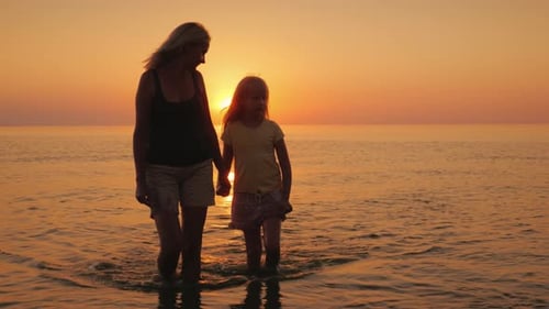 Mother and Daughter Walking in Ocean at Sunset