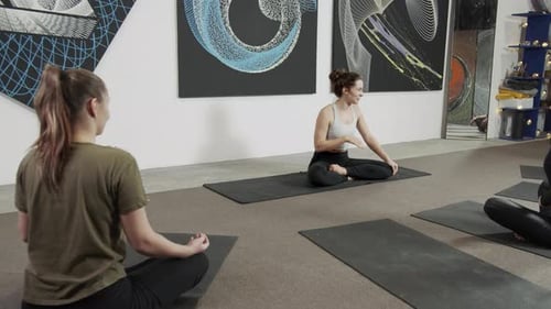 Healthy Young Women Waiting for a Yoga Class to Start in Light Loft Studio Sitting on Black Mats