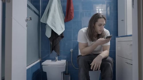 Young Caucasian Man Sending an Audio Message with His Phone in the Bathroom Frontal Shot