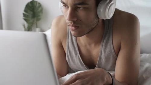 Man Works on Laptop While Lying in Bed
