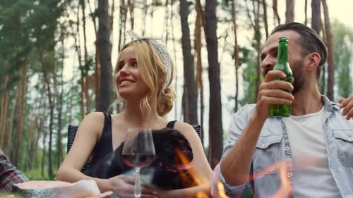 Friends Gather Around Campfire Enjoying Food and Drinks