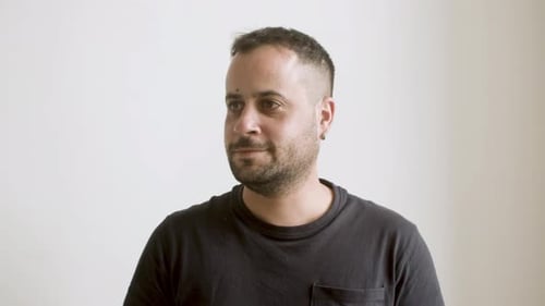 Man Smiling and Nodding in Front of White Wall