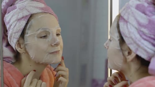 Woman Applying Cosmetic Face Mask in Bathroom. Skincare Spa. Facial Mask