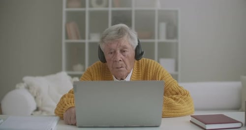Senior Man Using Laptop Wearing Headphones Indoors