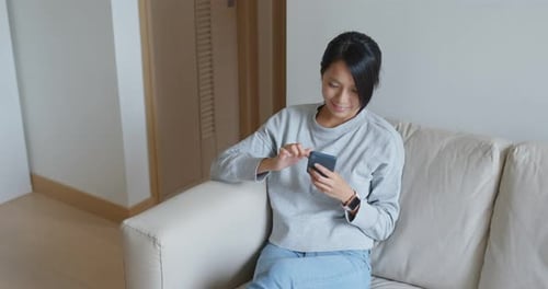 Woman Relaxes on Sofa Using Smartphone Device