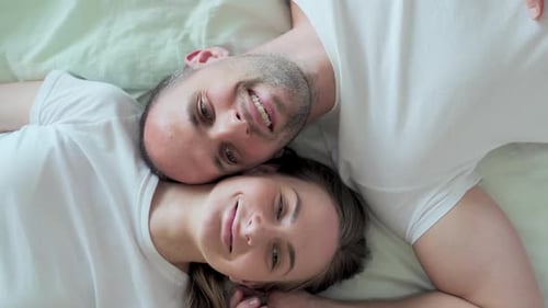 Liebevolles junges Paar küsst sich liebevoll, während es morgens gemeinsam von Angesicht zu Angesicht im Bett liegt