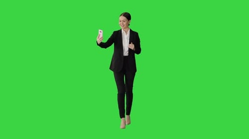 Young Female in a Suit Having Business Video Call on Her Phone on a Green Screen, Chroma Key.