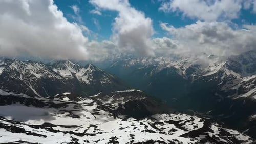 Air Flight Through Mountain Clouds Over Beautiful Snowcapped Peaks of Mountains and Glaciers