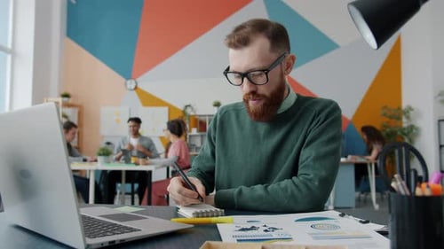 Handsome Young Man Concentrated on Business Activity Using Computer and Writing in Office