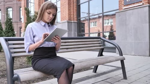Woman Using Tablet Sitting on Bench in Urban Park