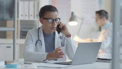 Female Doctor Using Laptop and Talking on Phone