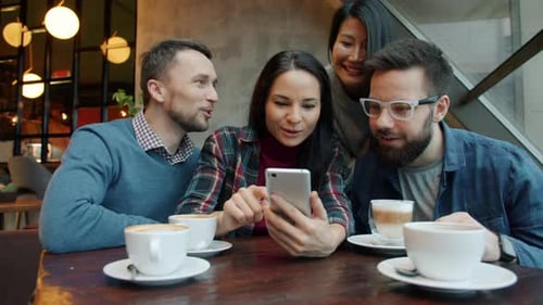 Asian and Caucasian Friends Using Smartphone Talking Smiling Having Fun in Cafe