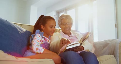 Grandmother and Granddaughter Reading Book on Couch Together