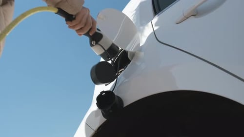 Bottom View of Woman Hand Inserts Power Cable Supply to Charge Electric or EV Car on the Background