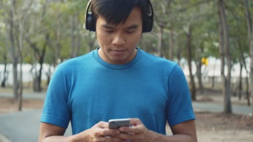 Young Man Listens to Music, Using Smartphone Outdoors