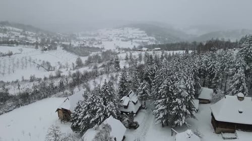 Snowy mountain aerial panoramic shot with wooden cabin and forest covered with snow.
