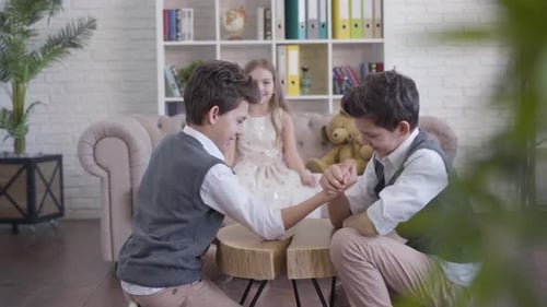 Stylish Caucasian Boys Competing in Armwrestling, Their Joyful Little Sister Cheering and Coming Up
