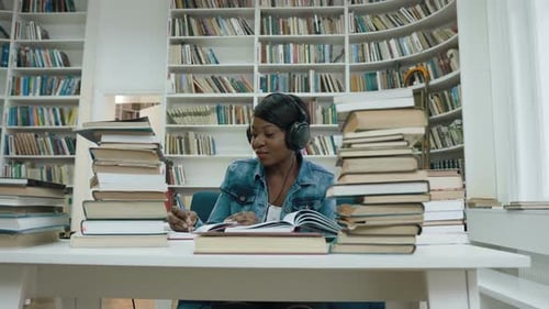 Glückliche afrikanische junge Frau hört Musik im Kopfhörer, während sie Vorlesung für die Universität schreibt
