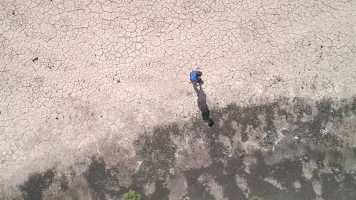 Top down view of woman walking across dry cracked desert viewing shadow