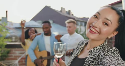 Femme asiatique avec un verre de vin faisant un selfie sur fond d'amis sur la terrasse
