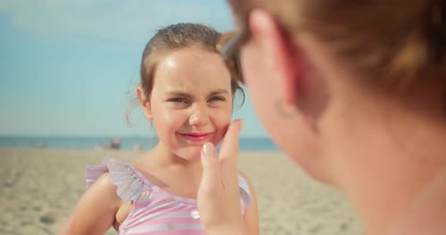 Mutter legt Sonnencreme auf das Gesicht ihrer Tochter, während sie im Sommer am Strand sitzt