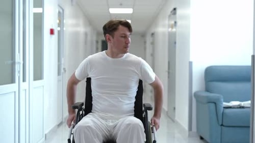 Man Rolling Wheelchair Along Hospital Corridor Looking Around