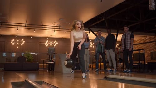 Eine junge Frau beim Bowling wirft einen Ball auf die Strecke und schlägt in Zeitlupe einen Schuss aus und springt