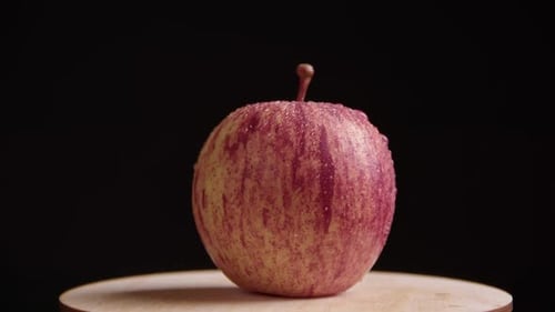 A juicy red apple rotates on a black background. Drops of water on a ripe fruit