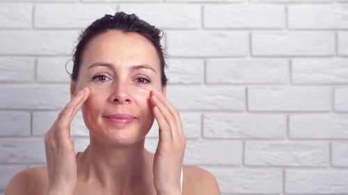 Woman Applying Lotion to Face, Beauty Treatment