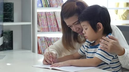 Asiatische Mutter hilft ihrem Sohn bei den Hausaufgaben auf weißem Tisch in Zeitlupe
