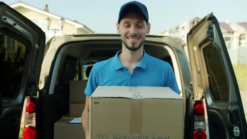 Slow Motion Portrait of Friendly Courier Holding Parcel with Goods Near Delivery Van