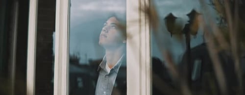 Joven mirando por la ventana, mirando hacia arriba, el reflejo de los edificios aparecen
