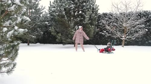 Young Happy Mother and Her Daughter Enjoying a Sledge Ride in a Beautiful Snowy Backyard