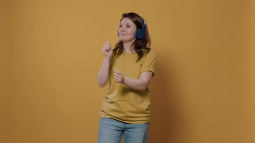 Woman Dancing with Headphones in Front of Yellow Background