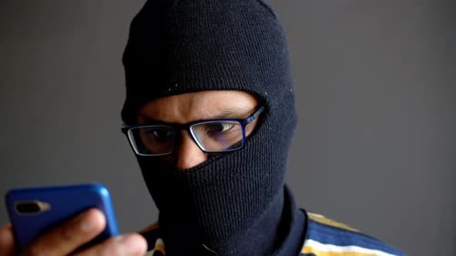 Masked Figure with Smartphone, Hacker Using Phone