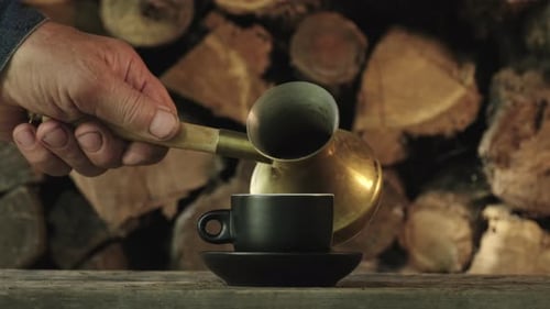 Pouring Coffee into a Cup by Firewood