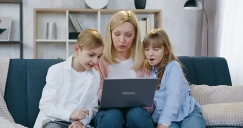 Familia de madre y dos hijos que se sientan juntos en el suave sofá de casa y usan la computadora