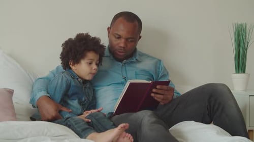 Father and Child Read Together on Bed