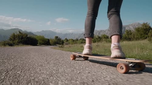 Close up female legs on longboard dreadlocks woman riding skateboard cruising downhill