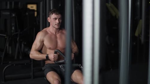 Athletic Man in the Gym Lifting Blocks on Rowing Machine Training on Block Device and Gym Equipment