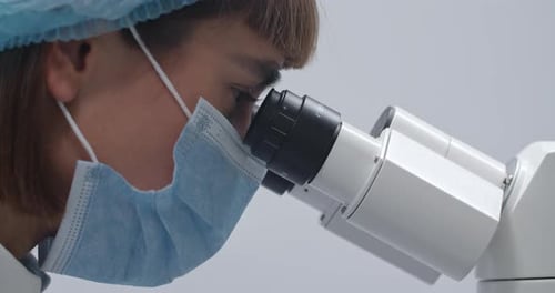 Crop View of Female Scientist in Bouffant Caplooking To Microscope