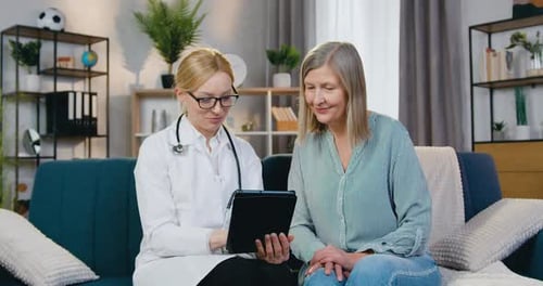 Doctor Reviews Tablet With Patient on Sofa
